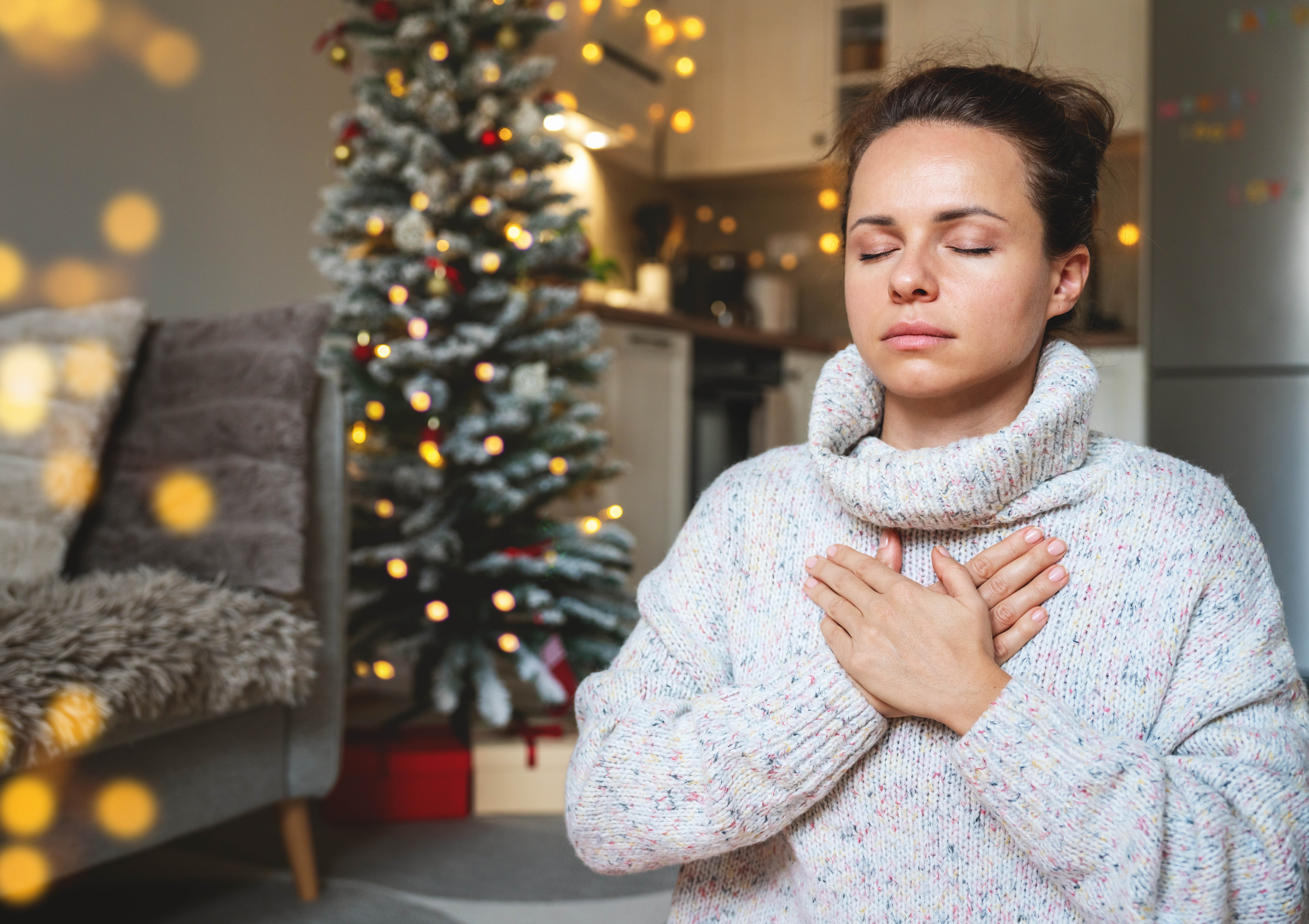 Woman with her eyes closed, hand on her chest, taking deep, relaxing breaths in front of the Christmas tree